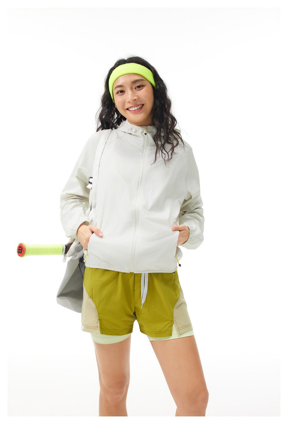 Front view of a model in an off-white hooded jacket and layered olive shorts with a neon yellow-green headband.