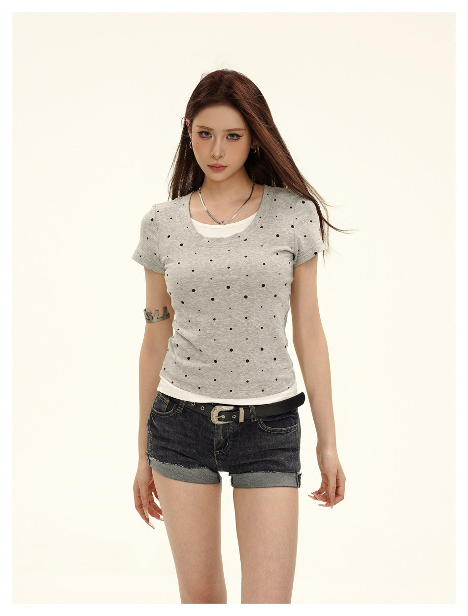Front view of a model wearing a light gray black-dotted tee over a white layer with dark cuffed denim shorts.