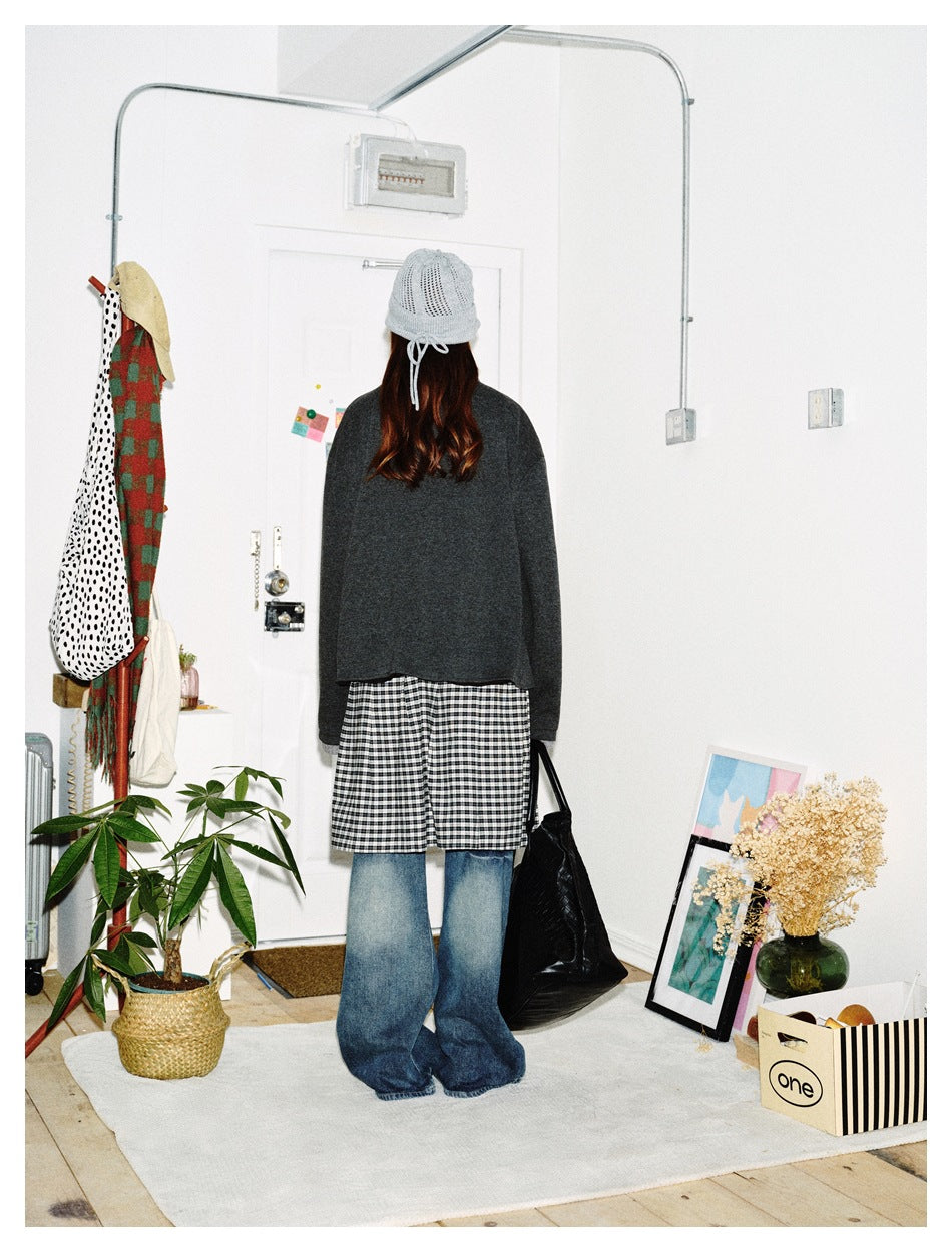 Back view of a model wearing the dark gray jacket with a plaid skirt, jeans and a gray knit beanie