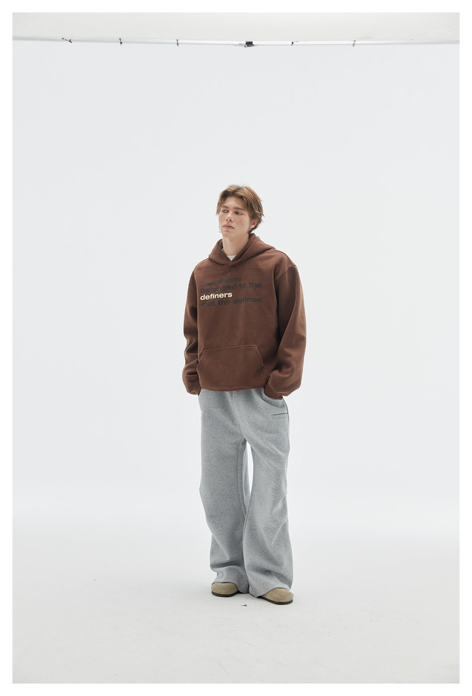 Full-length front view of a model wearing a brown text-print hoodie and loose gray pants.