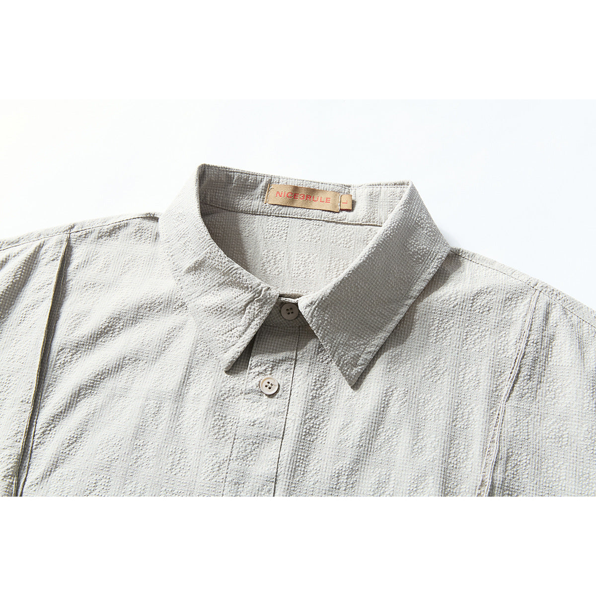 Close-up of a pale gray short-sleeve shirt's pointed collar, buttons, and textured geometric fabric.