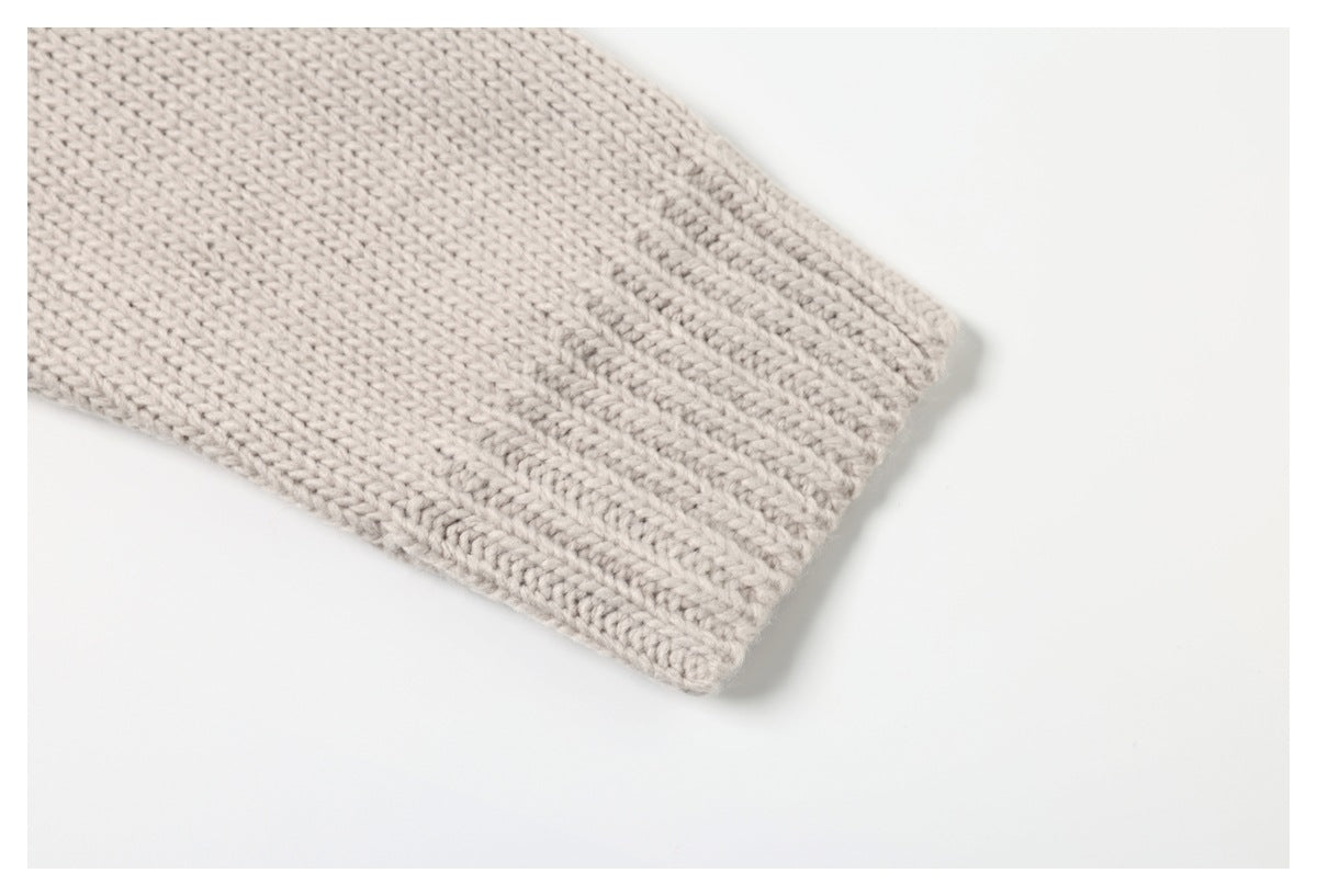 Close-up of a cream sweater sleeve ending in a ribbed knit cuff on a white background.