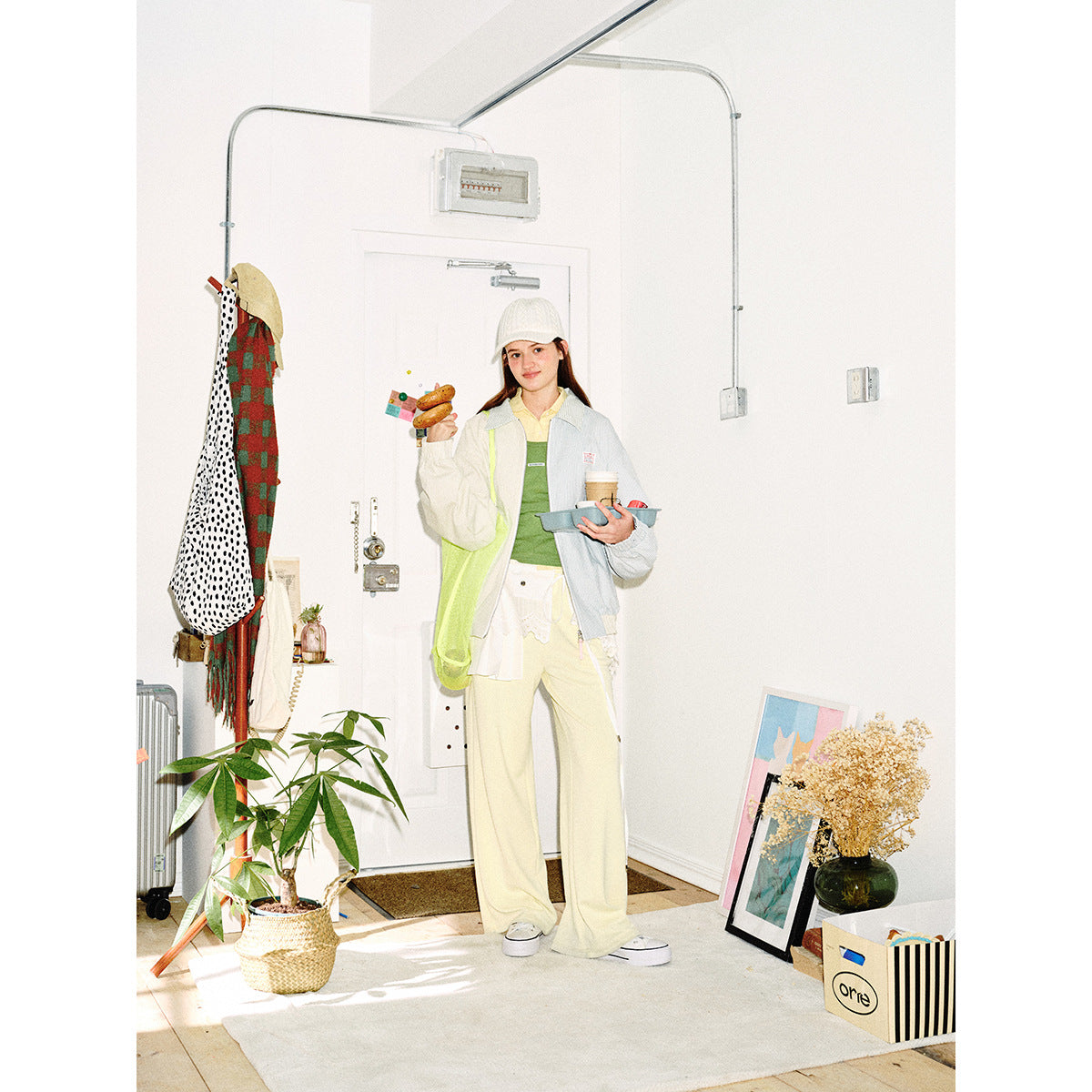 Model wearing a pale blue and cream pinstriped zip jacket with a green top and cream trousers in a bright entryway.