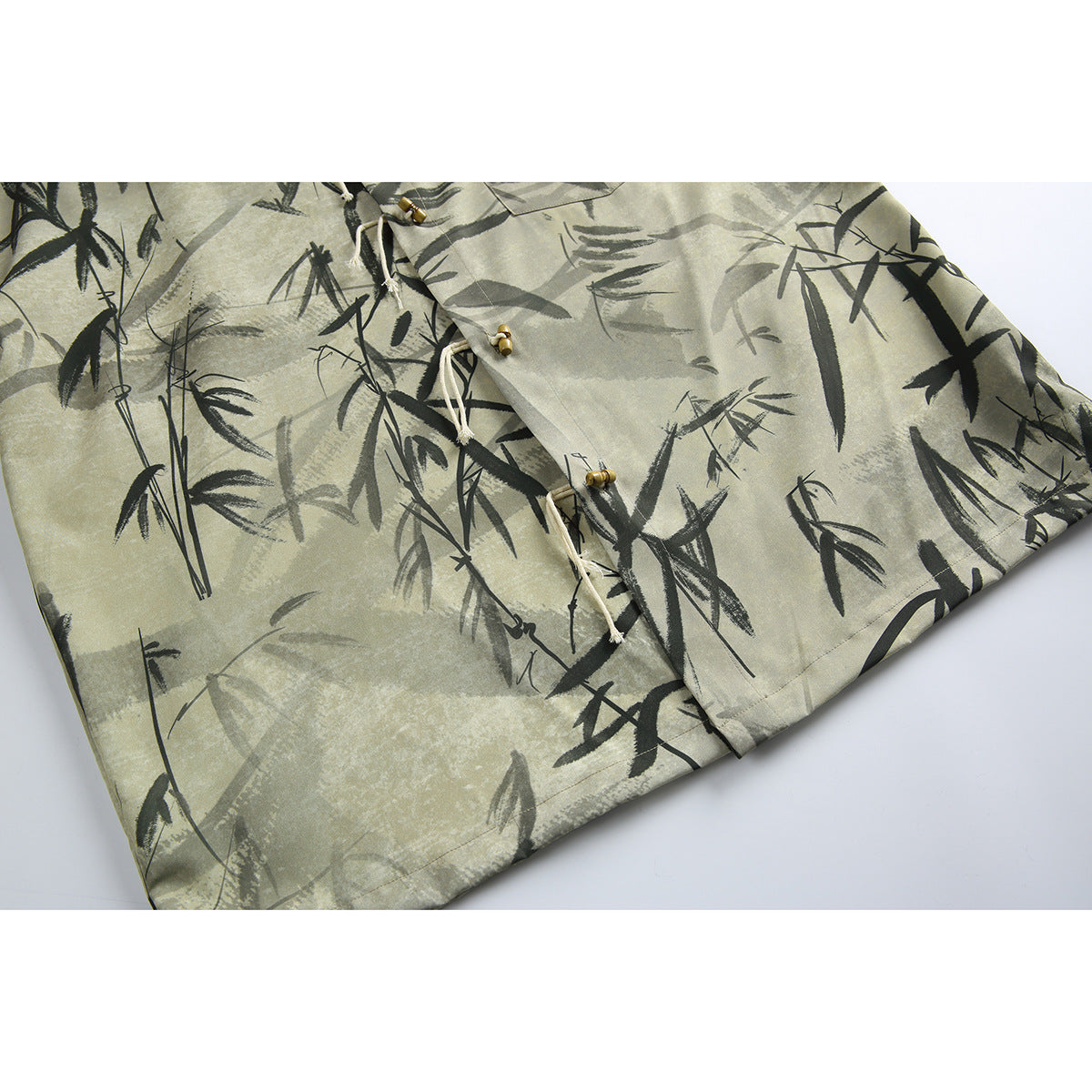 Close-up of a beige-gray bamboo-print shirt showing its front toggles, cream ties, short sleeve, and hem.