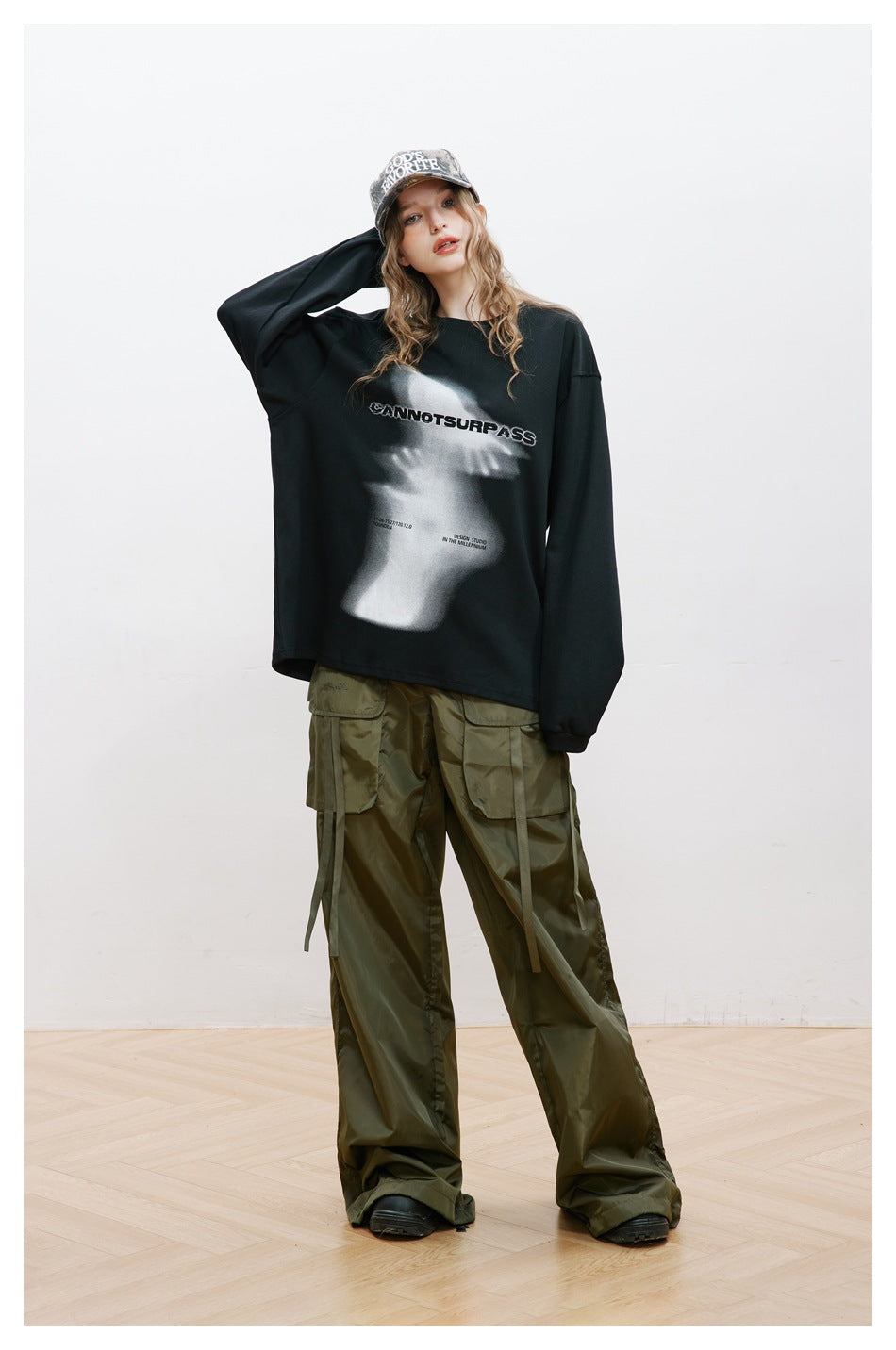Model wearing a black oversized long-sleeve top with a gray graphic and olive cargo pants.