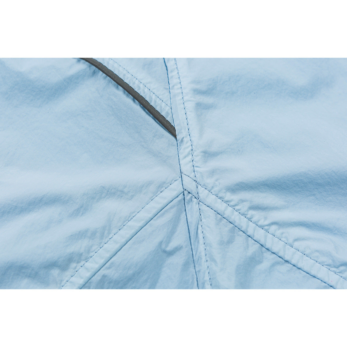 Close-up of light blue jacket fabric with intersecting stitched seams and dark edge trim.