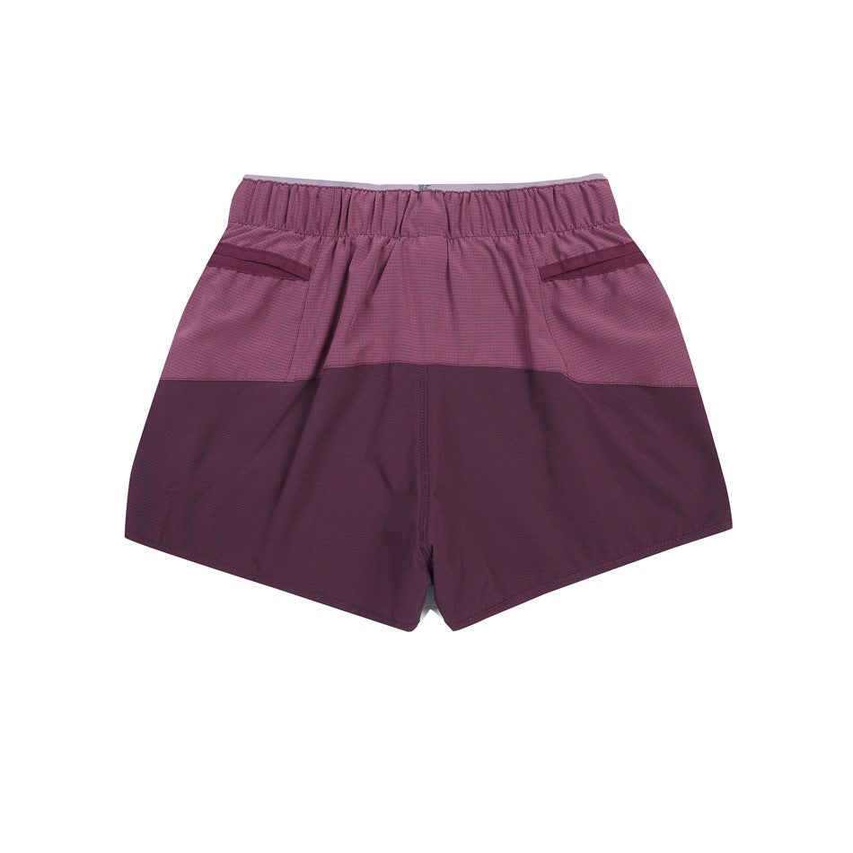 Back view of color-block athletic shorts in dusty rose and deep plum with an elastic waistband and angled pocket openings.