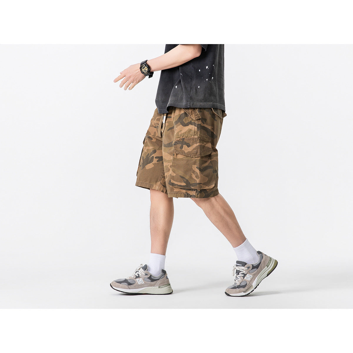 Model in brown camouflage cargo shorts with large side pockets, shown in a walking pose.