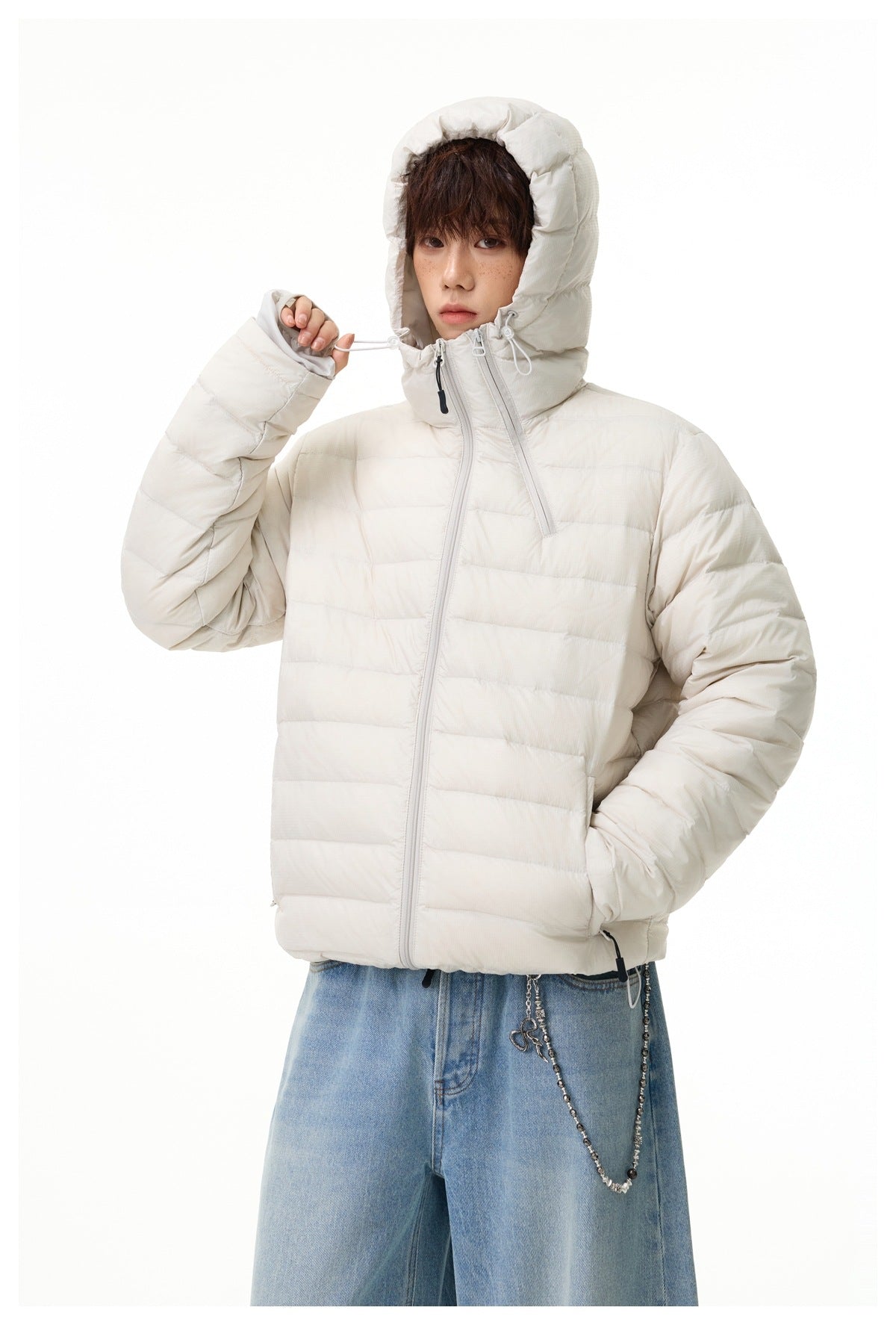 Model wearing off-white hooded quilted jacket with the hood up, holding a drawcord, with light-wash jeans