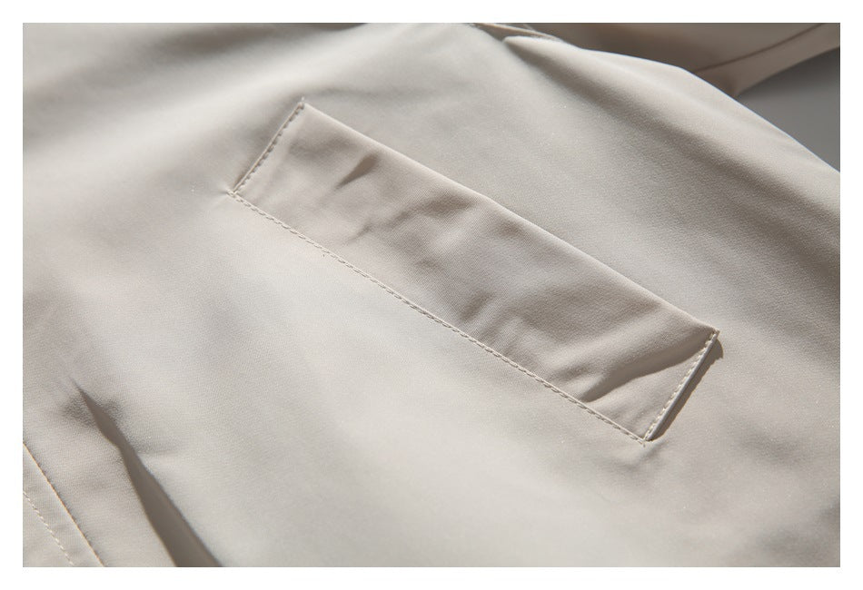 Close-up of a beige jacket's stitched rectangular pocket on smooth fabric.