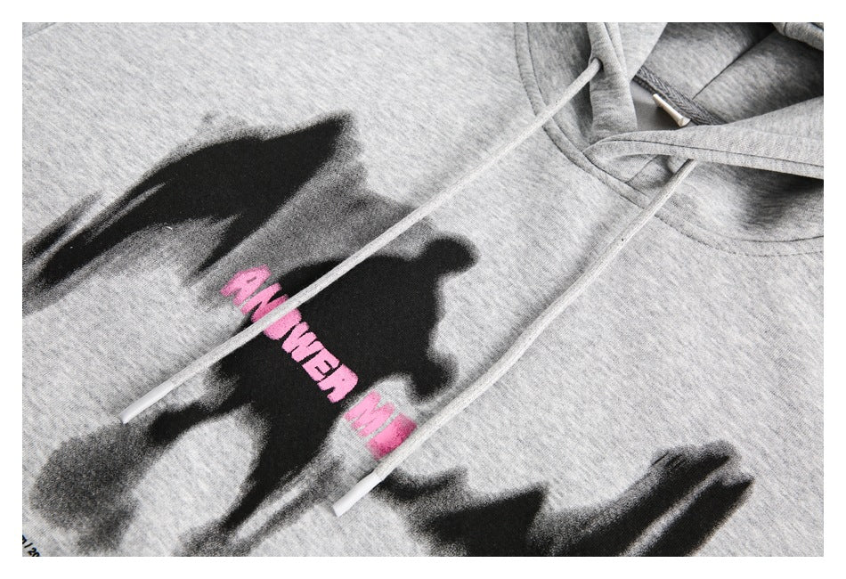 Close-up of the gray hoodie’s black brushstroke chest graphic, pink lettering, and drawstrings.