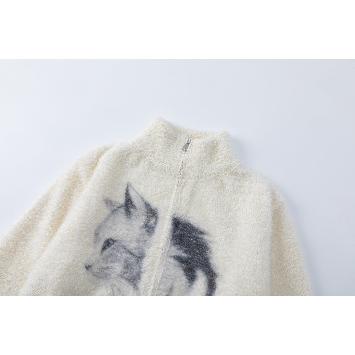 Close-up of a cream fuzzy zip-up sweater with a high collar and a grayscale cat graphic on the front.