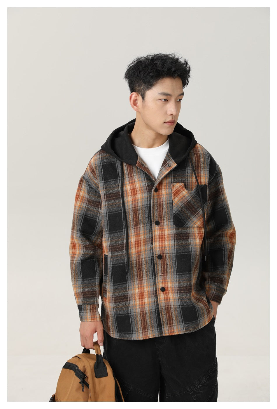 Closer view of a man wearing a black, gray, and orange plaid hooded overshirt with a button front and chest pocket.