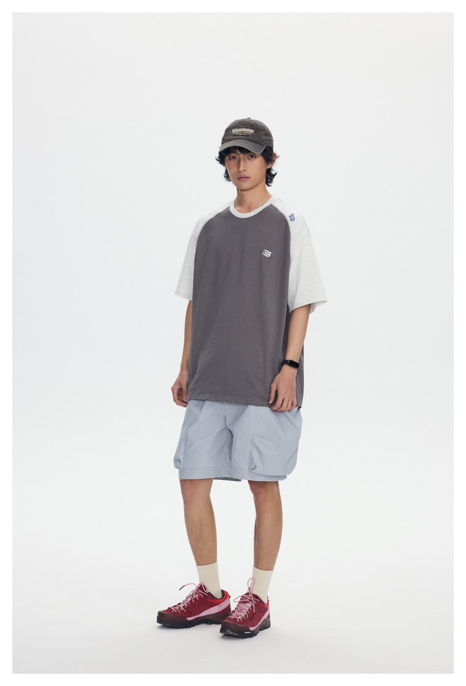 Full-length front view of a model wearing a charcoal T-shirt with light gray raglan sleeves and pale blue shorts.