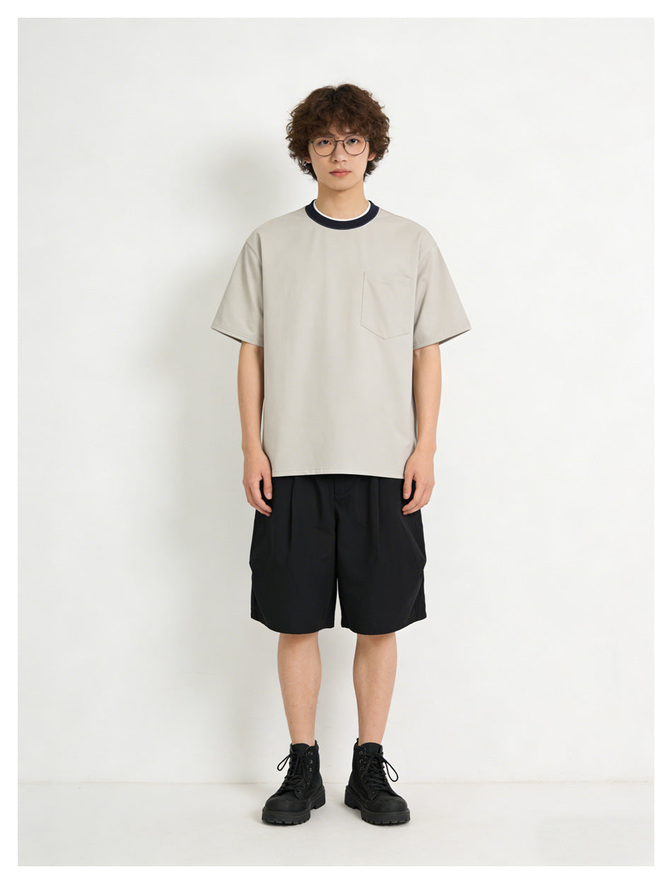 Front view of a model wearing a light gray short-sleeve T-shirt with a chest pocket and dark contrast collar, paired with