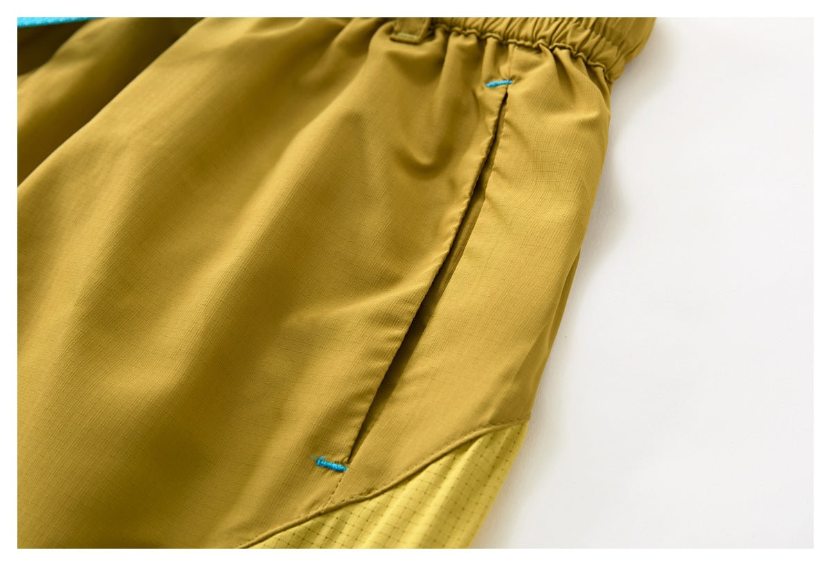 Close-up of mustard-yellow garment with an elasticized edge, a slanted pocket opening, and blue bar-tack stitching.