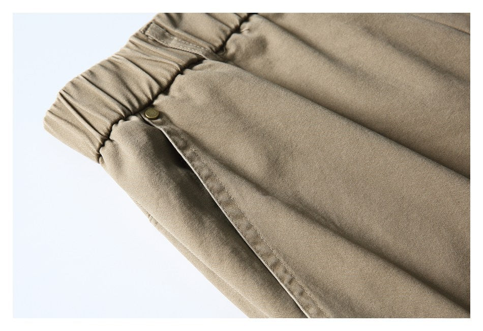 Close-up of taupe trousers showing the gathered waistband and a side pocket with a snap.
