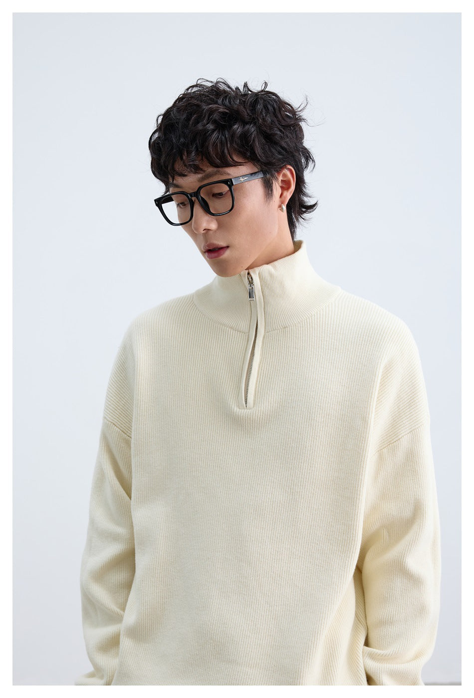 Close view of a model wearing an ivory ribbed pullover with a high collar and short zipper.