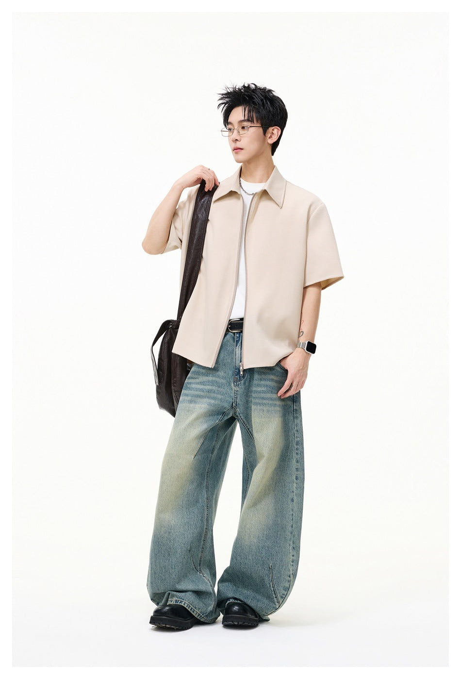 Model wearing a light beige short-sleeve zip-front collared shirt over a white tee with loose blue jeans.