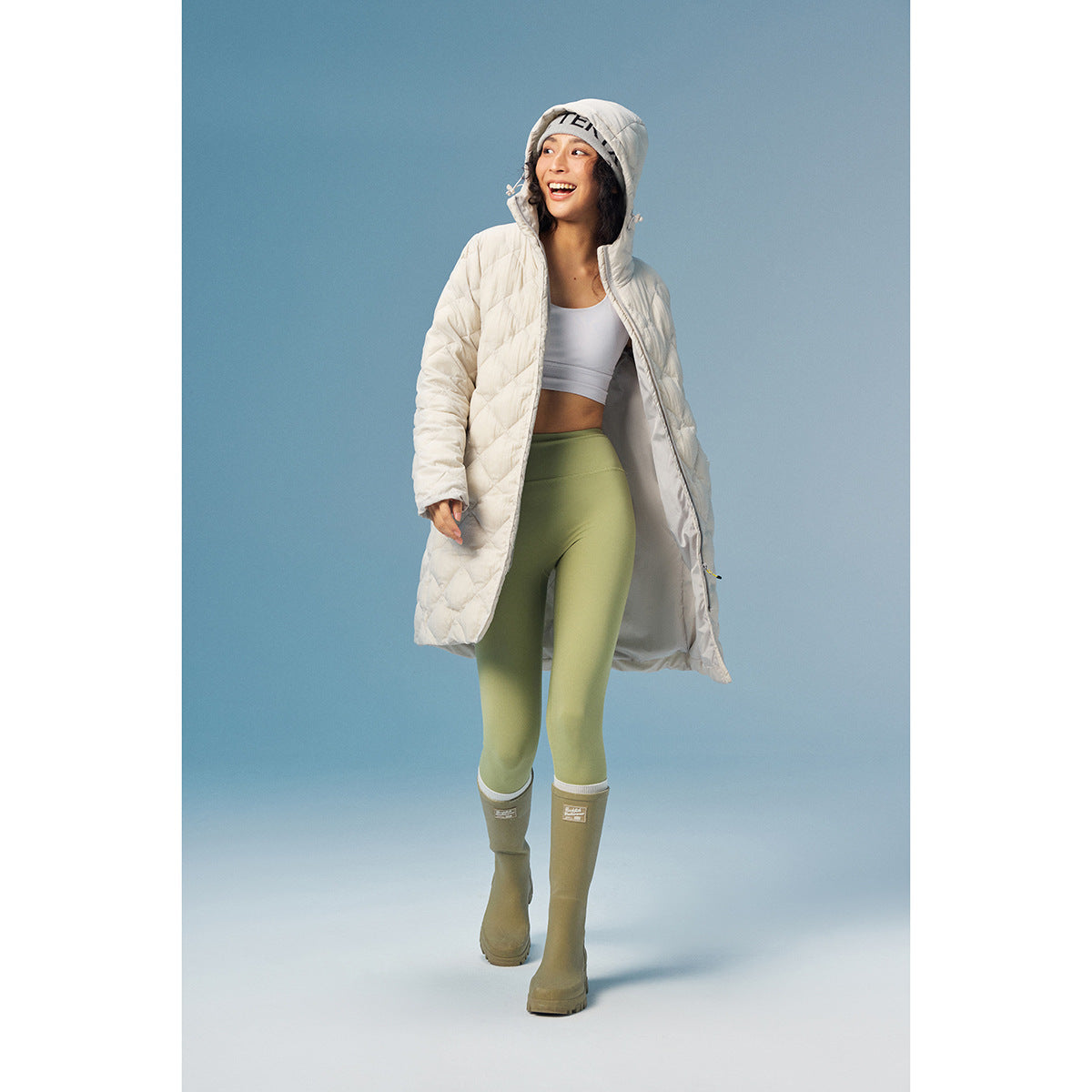 Woman wearing an open white hooded quilted coat with a longline cut, white top, and olive leggings.