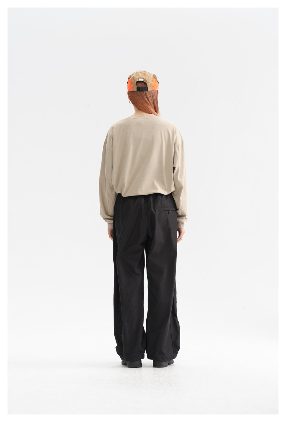 Back view of a model wearing loose black pants and a beige long-sleeve shirt, with a rear pocket.
