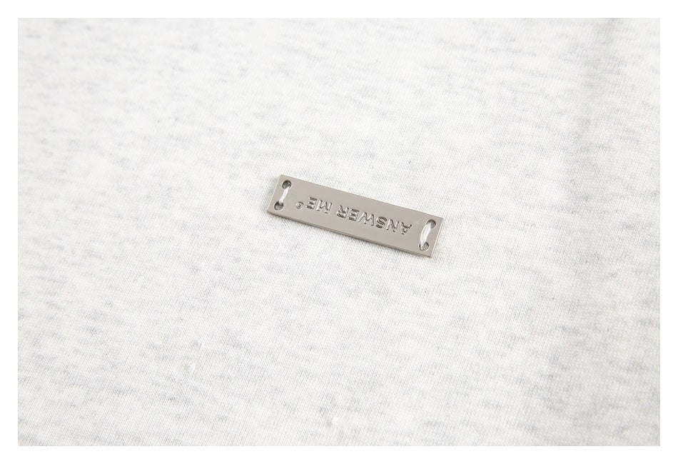 Metal ANSWER ME plaque attached to light gray fabric.