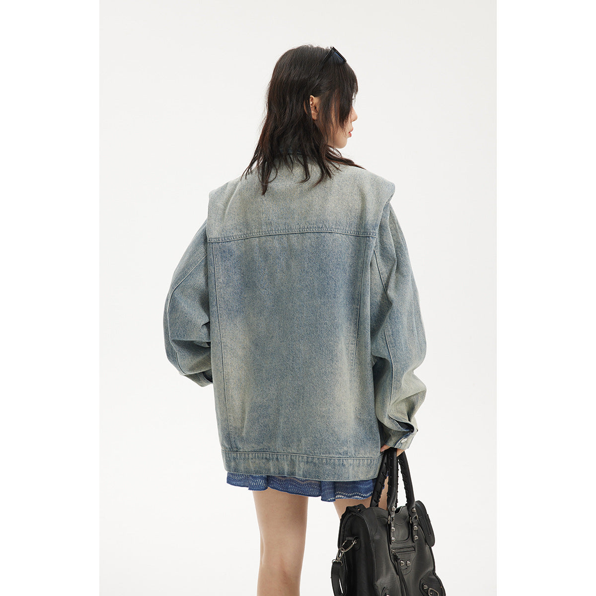 Rear view of a model wearing an oversized, faded light blue denim jacket; a blue patterned dress is visible below the hem.