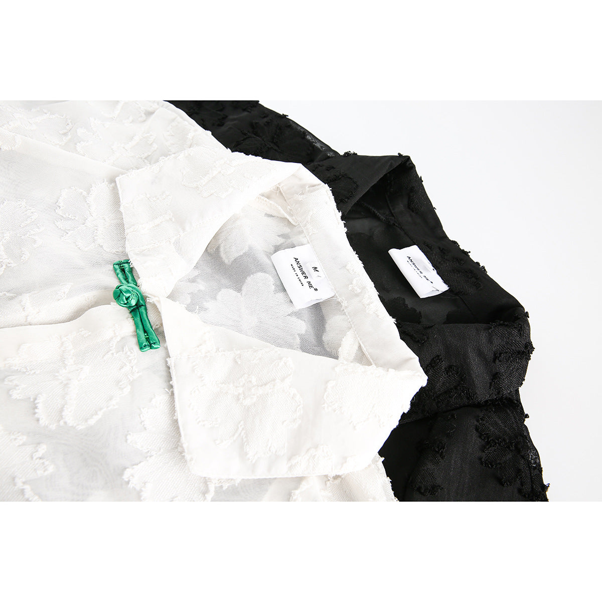 Close-up of white and black textured shirts with bright green frog closures and inner neck labels.