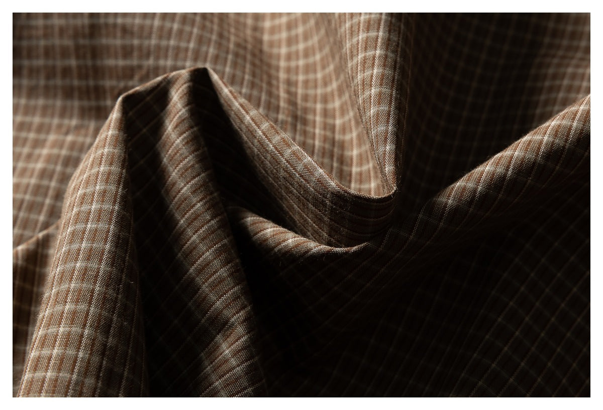 Close-up of brown checked fabric draped into folds, showing its fine grid pattern.