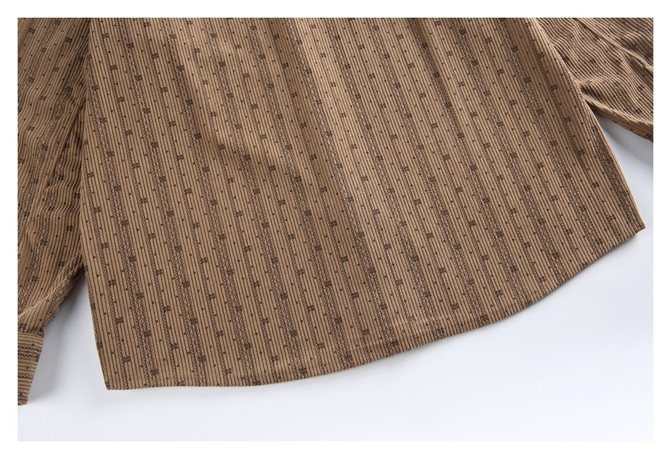 Cropped flat lay of a brown long-sleeve garment with vertical ribs, scattered dark motifs, and a curved hem.