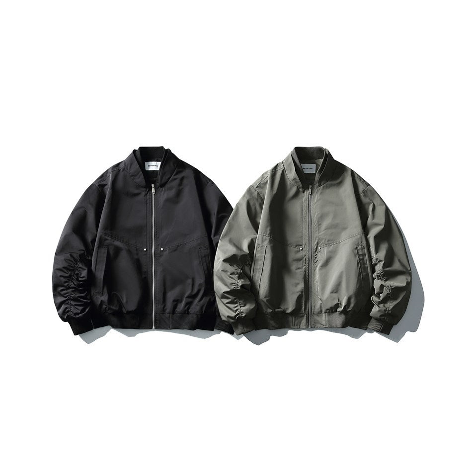 Front view of two zip-front bomber jackets, one black and one olive gray, displayed side by side.