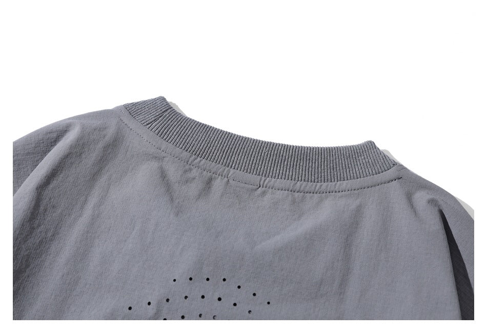 Close-up of a gray garment's ribbed crew neckline and small black dot pattern.