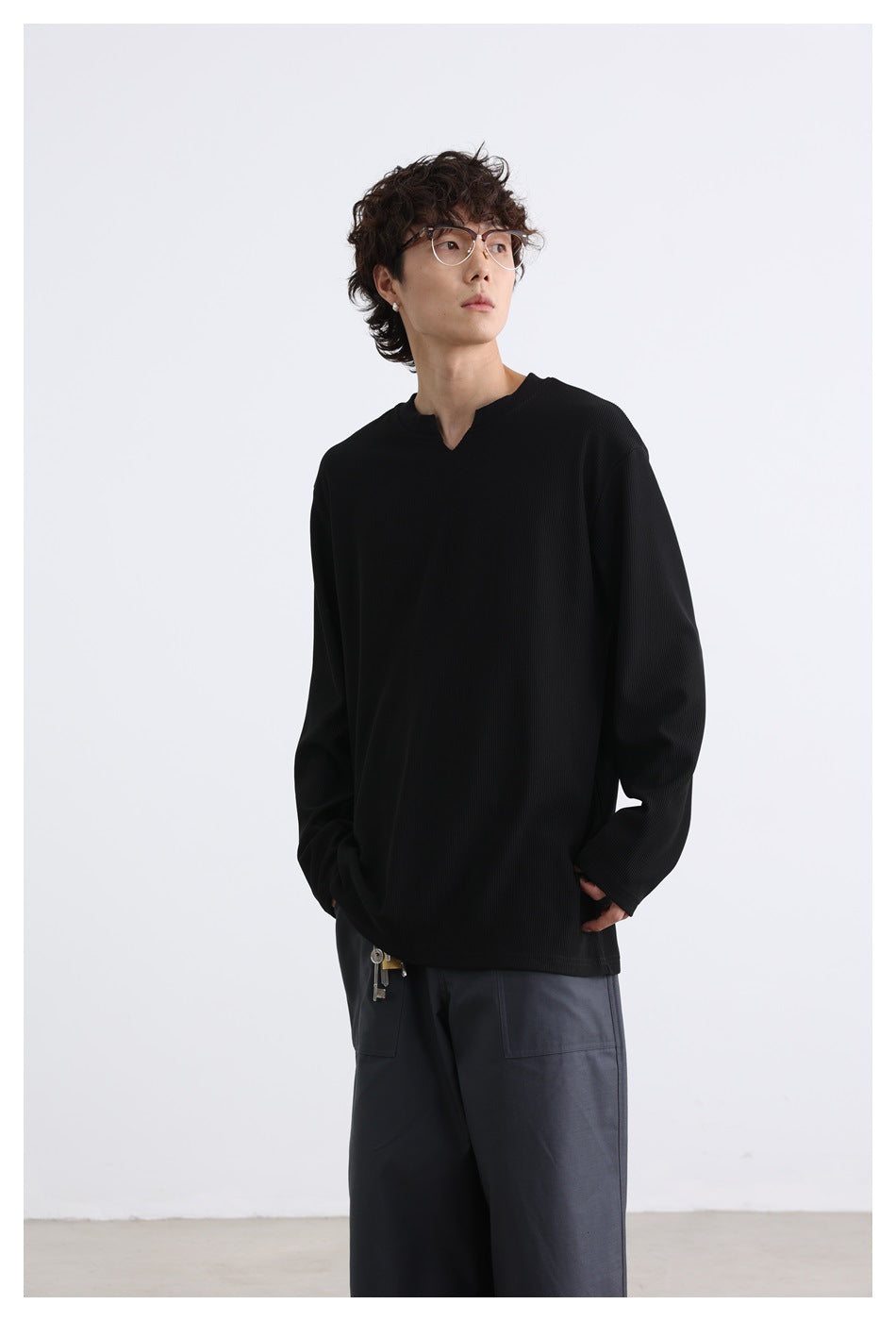 Model wearing black ribbed long-sleeve top with notched V-neck and gray pants, upper-body view