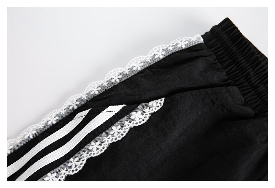 Close-up of black pants with an elastic waistband, white striped trim, and floral lace edging.