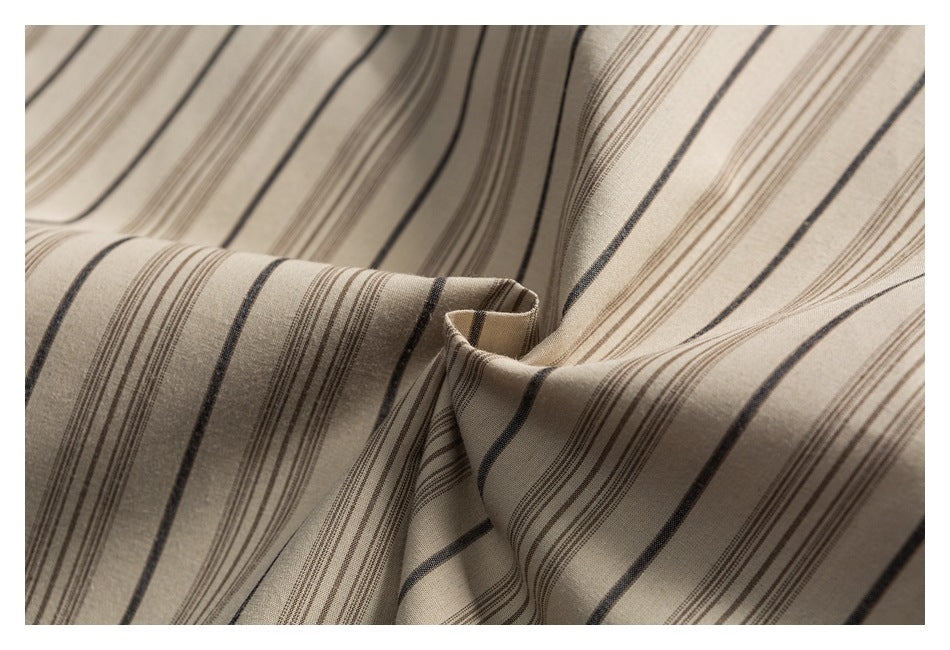 Close-up of beige fabric with narrow brown and dark gray stripes draped into soft folds.