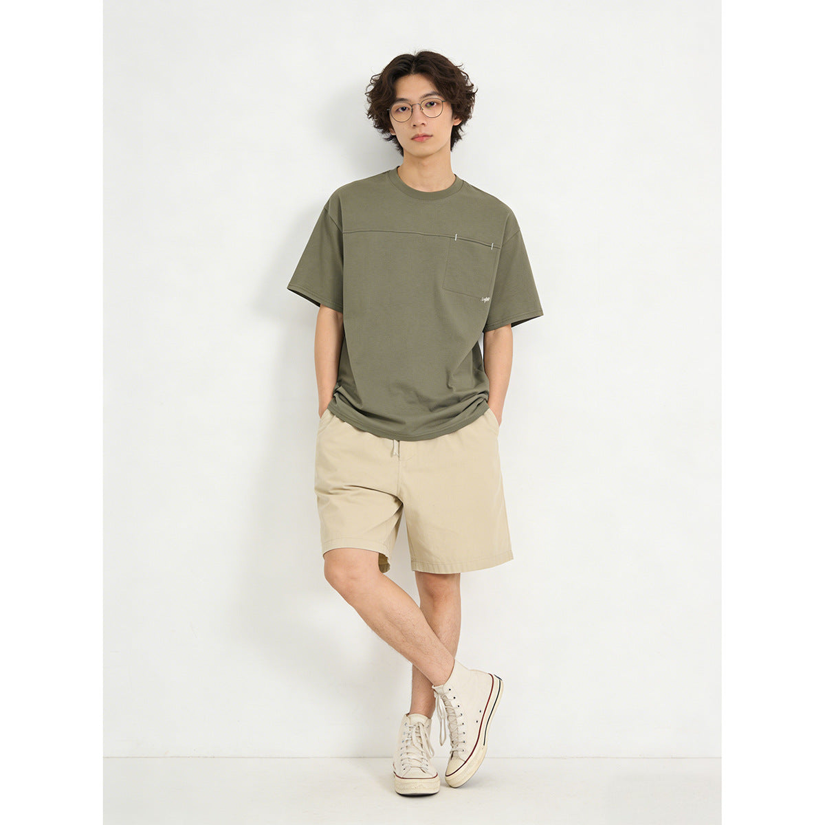 Model wearing an olive short-sleeve T-shirt with a chest pocket and beige shorts.