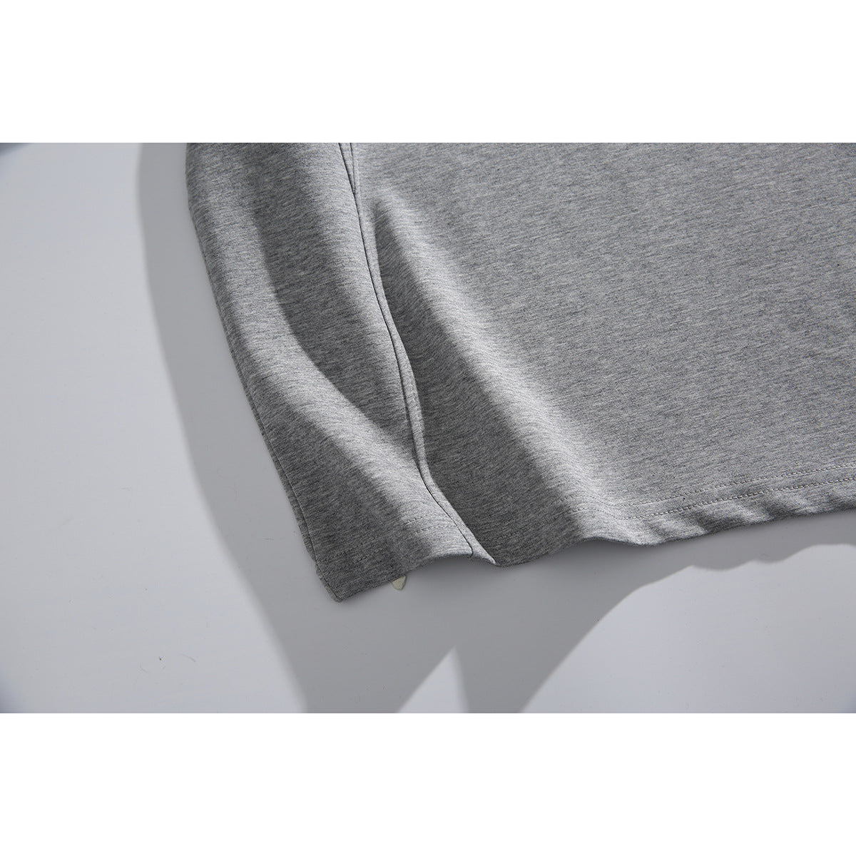 Close-up of the gray top's sleeve and stitched hem on a light background.