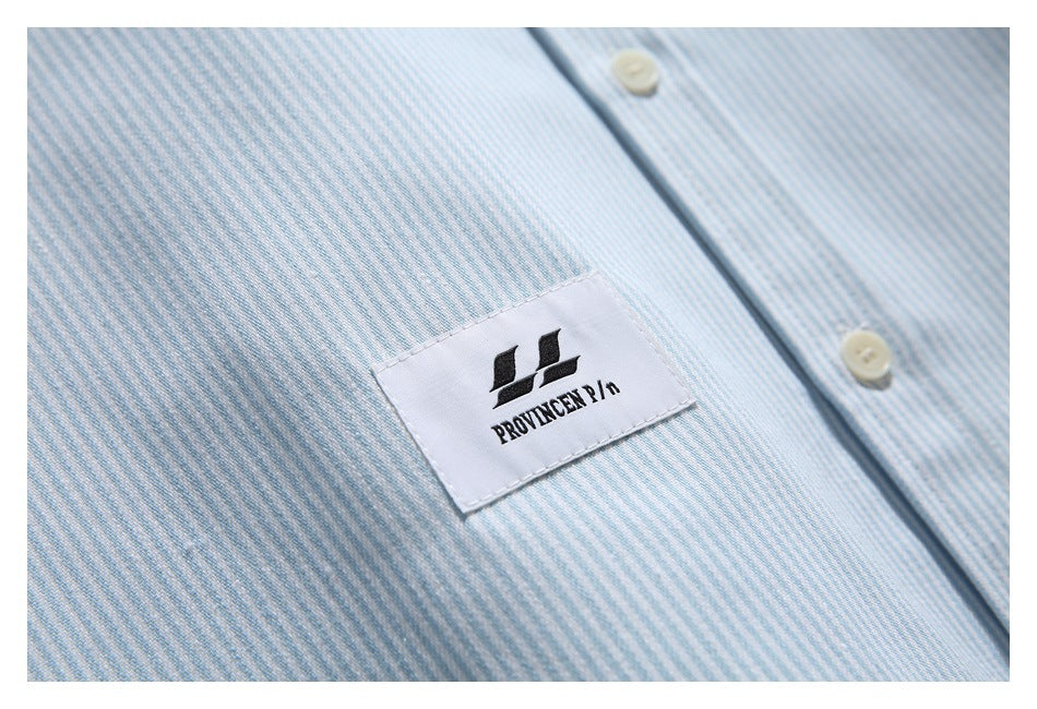 Close-up of a sewn logo label on the light blue and white striped shirt.