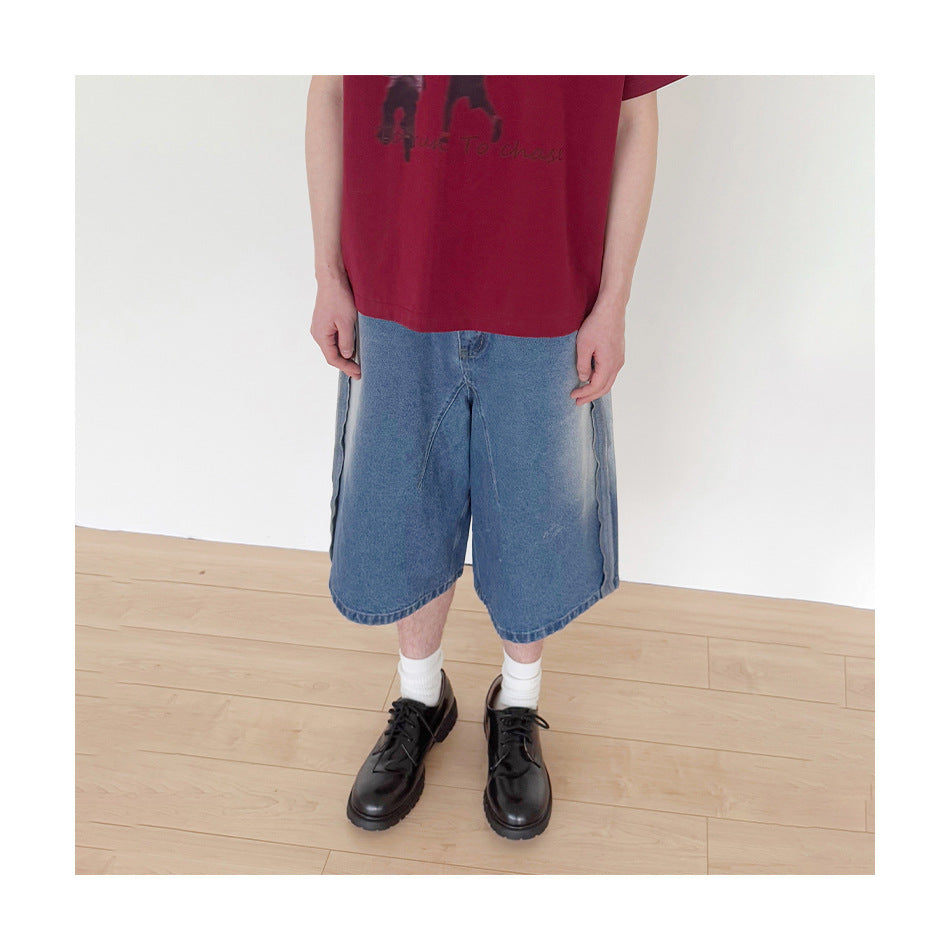 Cropped model wearing loose, knee-length blue denim shorts with pale side panels and a burgundy graphic T-shirt.