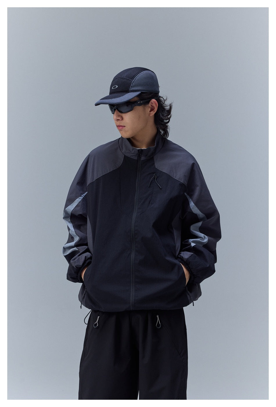 Closer view of a model wearing a charcoal and black color-block zip jacket with a high collar and zip pockets.