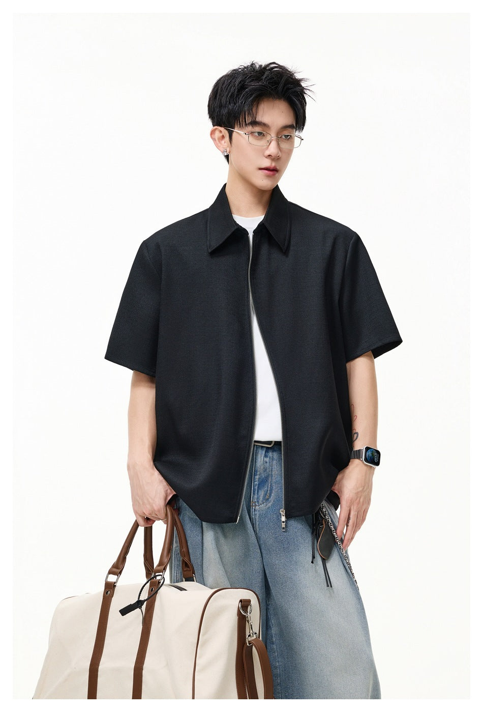 Front view of a model wearing a black short-sleeve zip-front shirt with a pointed collar and loose blue jeans.