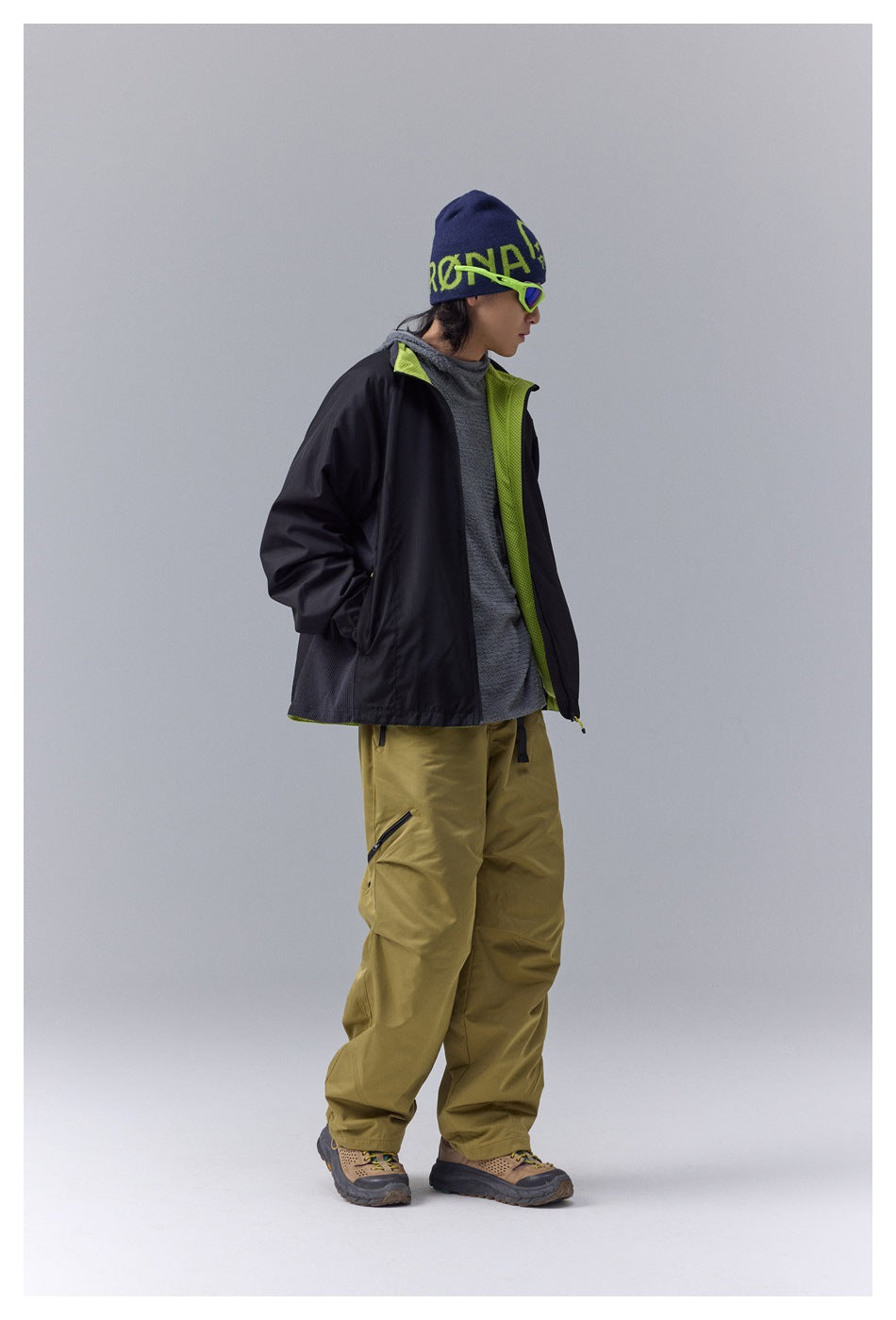 Model wearing a black jacket with lime lining and olive pants, shown in side profile.