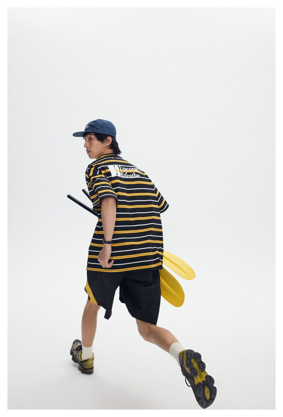 Model in a striped black T-shirt shown from behind, with a large white back print and black shorts.