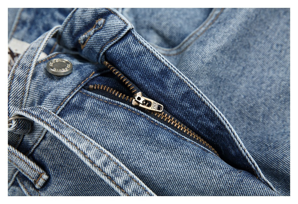 Close-up of blue jeans with the fly unfastened, showing the metal zipper, button, and belt loop.