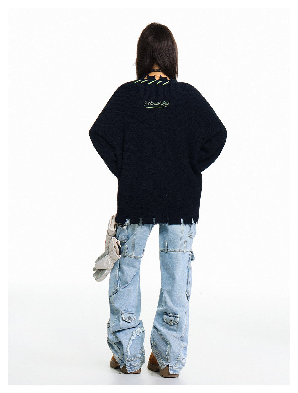 Back view of a model wearing a dark navy oversized sweater with a distressed hem, green stitching, and small embroidered
