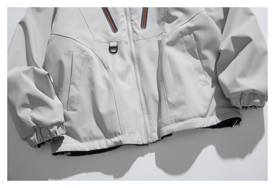 Close-up of a light gray jacket showing lower pockets, center zipper, D-ring and elastic cuffs.