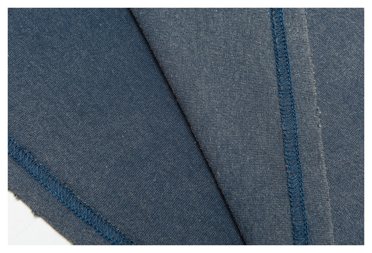 Close-up of dark blue-gray garment fabric with a diagonal seam and blue overlock stitching.