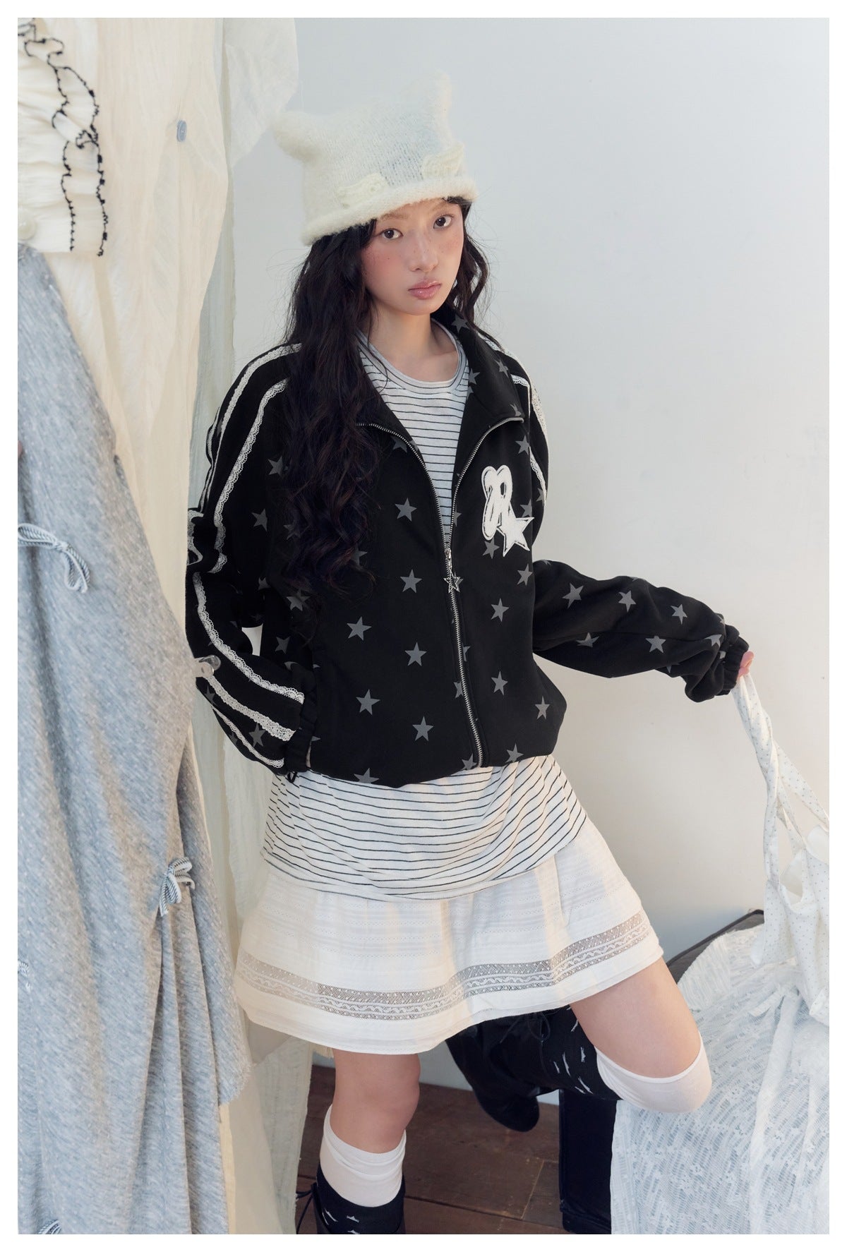 Model wearing a black star-print zip jacket with white lace sleeve stripes and a chest patch, shown with a striped top and