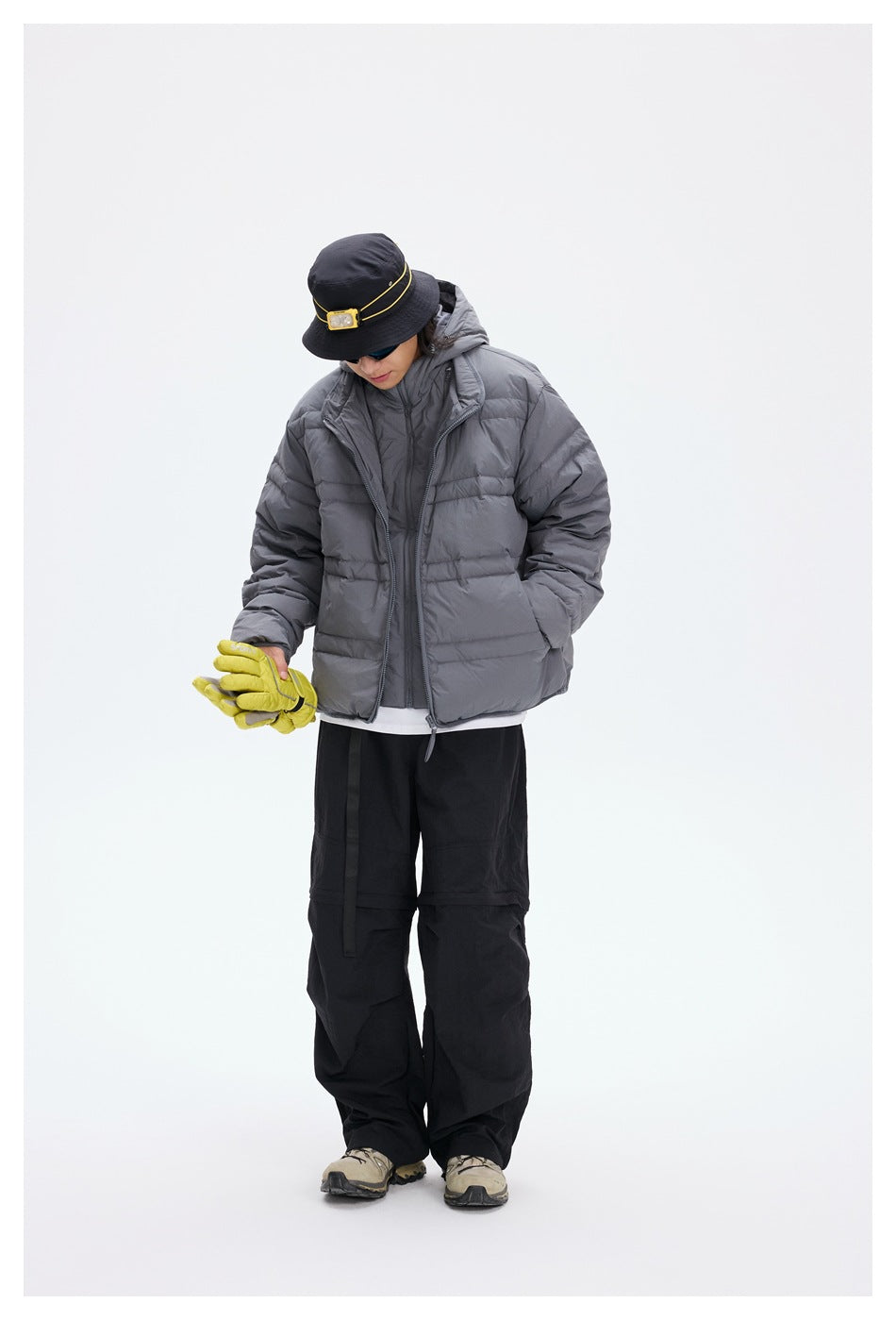 Model wearing a gray hooded quilted jacket over a second layer, with black trousers.