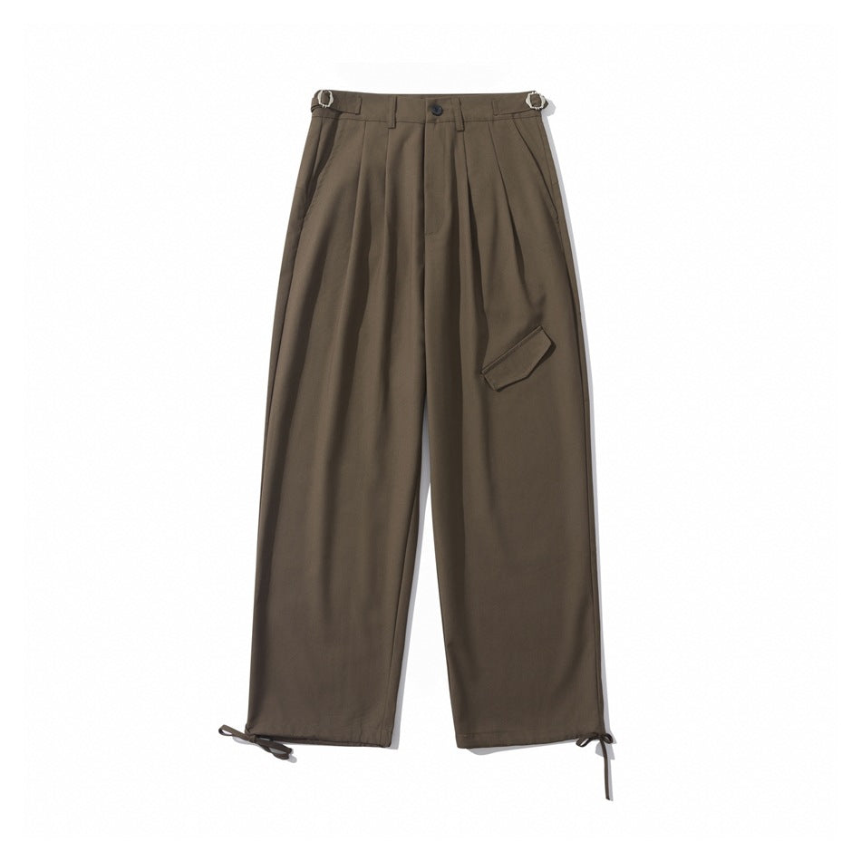 Brown wide-leg pleated trousers flat lay with side buckle tabs, front flap detail and hem ties